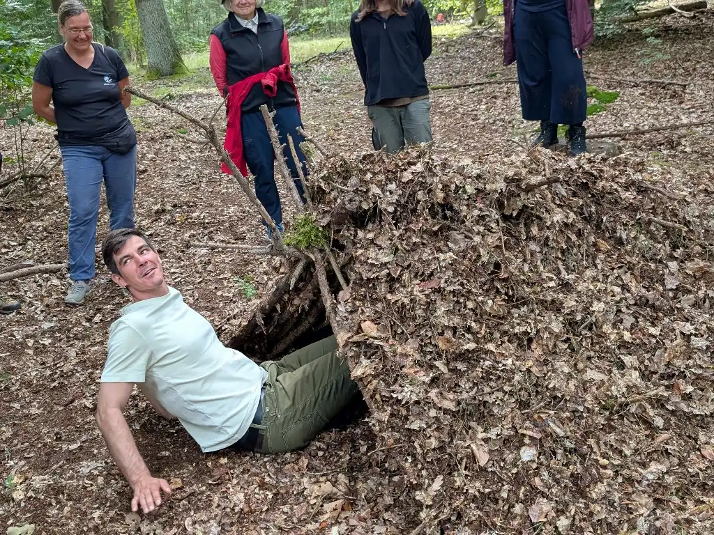 Ein Mann liegt in einer selbstgebauten Laubhütte im Wald bei einem Teamtag.