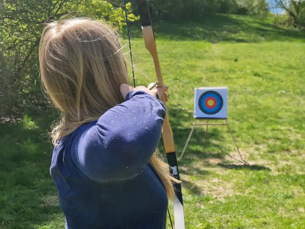Ein Junge schießt einen Bogen auf einer Waldwiese.