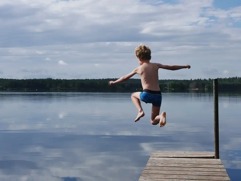 Ein Junge springt vom Steg ins Wasser.