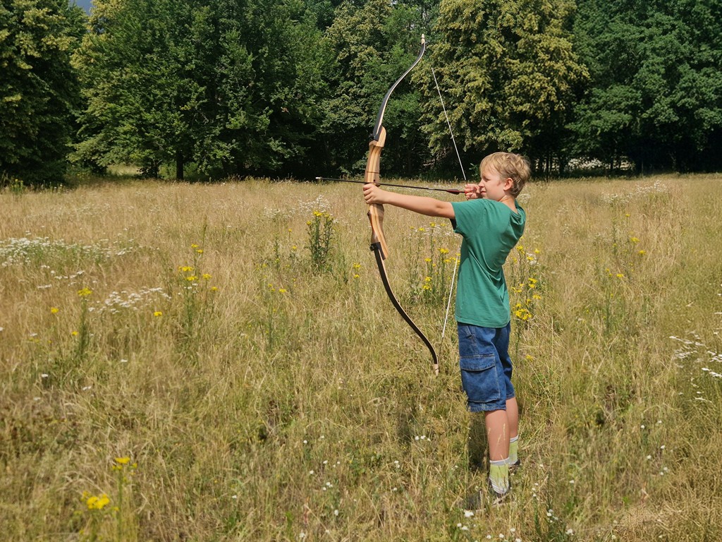 Ein Junge schießt einen Bogen auf einer Waldwiese.