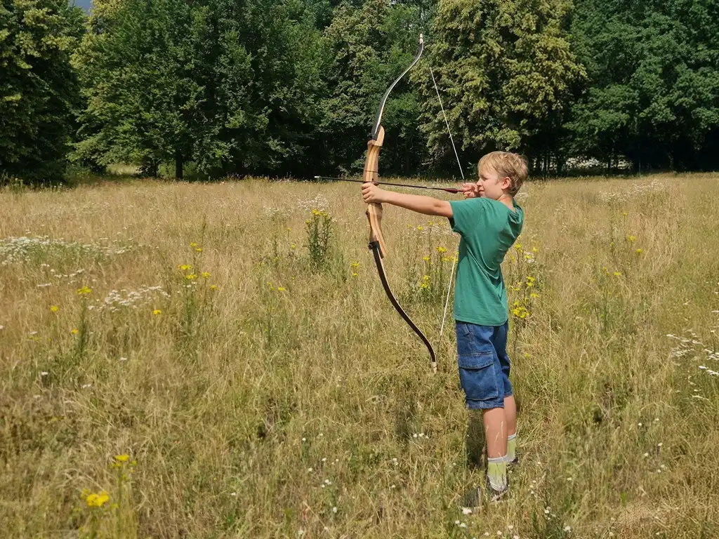 Ein Junge schießt einen Bogen auf einer Waldwiese.