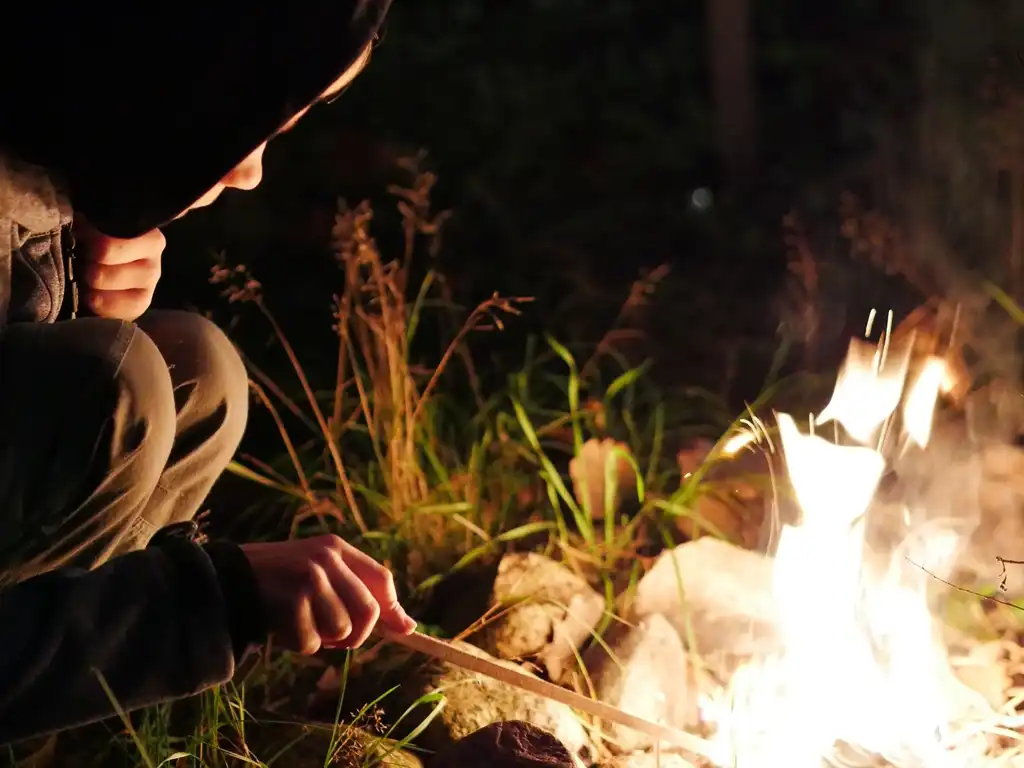 Ein Junge hütet im Dunkeln ein Feuer.