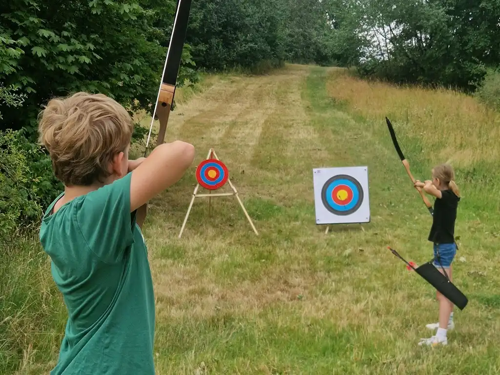 Kinder üben im Feriencamp das Bogenschießen.