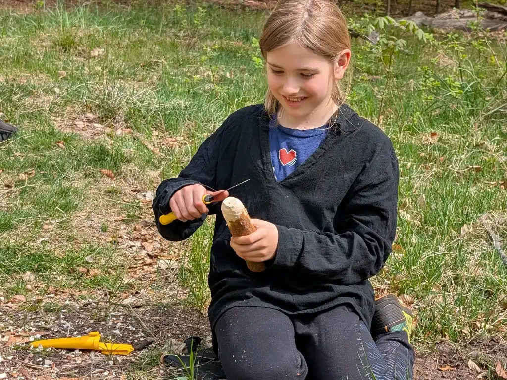 Ein Kind schnitzt im Wald beim wilden Kindergeburtstag.