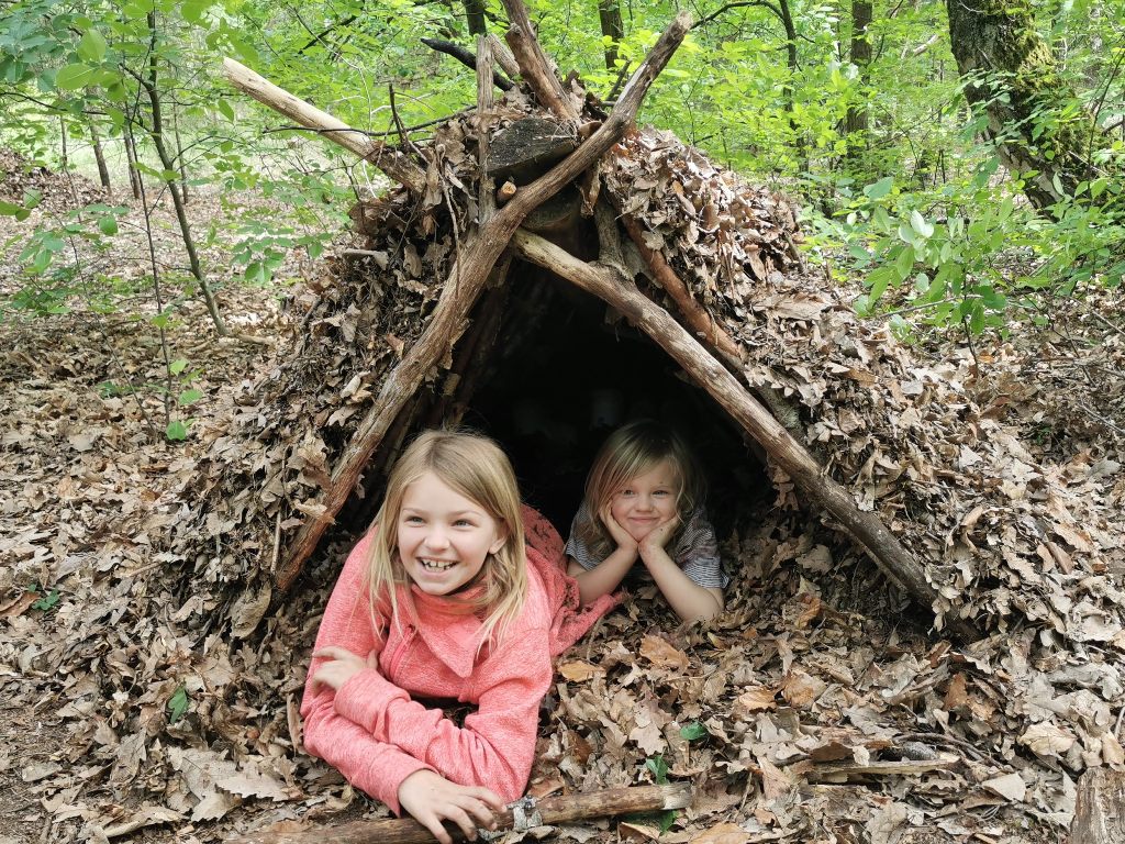 Zwei Kinder liegen in ihrer selbstgebauten Laubhütte im Wald.
