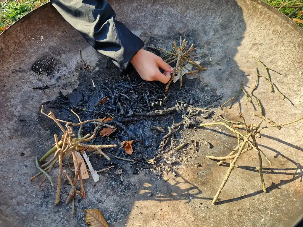 In einer Feuerschale wird ein Stöckertipi aufgebaut.